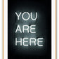 A black and white, scandi typography wall art with YOU ARE HERE neon letter lighting installation on a black wall background. 